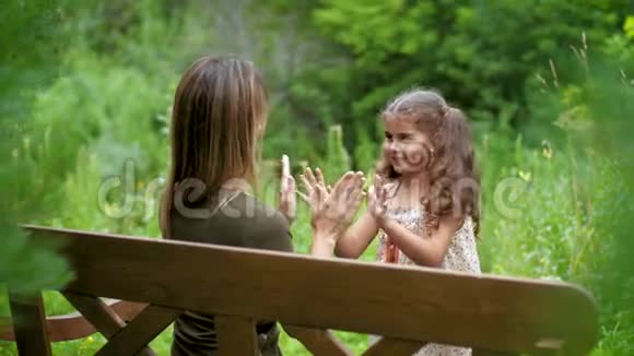妈妈坐在树间的长凳上她和孩子玩小蛋糕女人带着孩子玩无忧无虑的笑视频的预览图