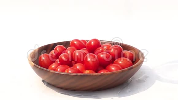 在白色背景的木碗里往一堆樱桃番茄上浇新鲜水视频的预览图