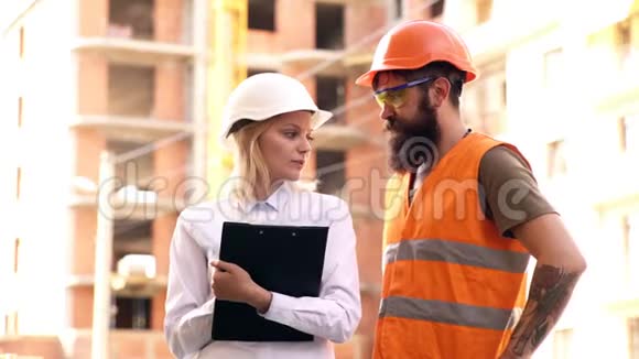 戴着防护头盔的妇女与戴着头盔和穿着防护背心的建筑工人沟通视频的预览图