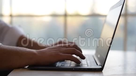 特写男人的手在笔记本电脑键盘上打字在窗口的背面视频的预览图