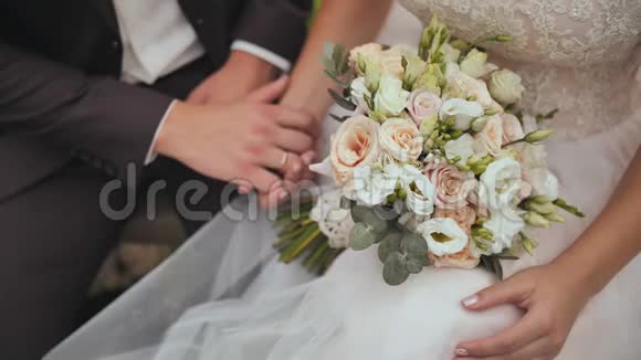 新娘和新郎坐着轻轻地互相抚摸手和婚礼花束的特写视频的预览图