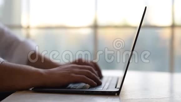 特写男人的手在笔记本电脑键盘上打字在窗户的背面视频的预览图