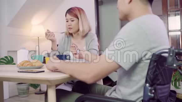 快乐甜蜜的亚洲夫妇男人坐在轮椅上吃早餐牛奶中的谷类食品面包和喝橙汁视频的预览图