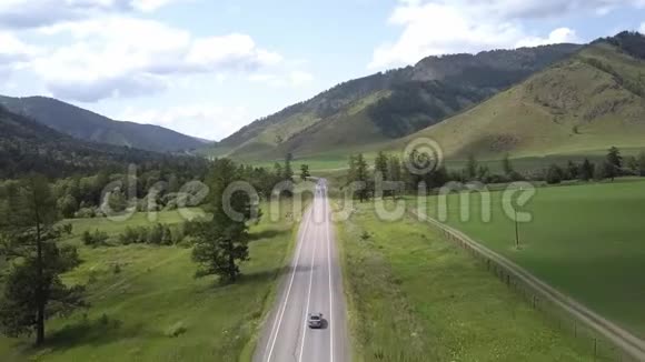 空中飞行在田野和山脉之间的道路上夏日阳光明媚在路上路过汽车阿尔泰共和国视频的预览图