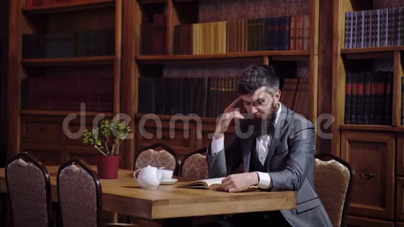 商人坐在复古的内部拿着书和一杯茶长胡子的人穿着豪华西装在他的内阁奢华视频的预览图