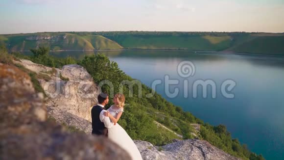 一对夫妇轻轻拥抱站在悬崖边上看着湖面视频的预览图