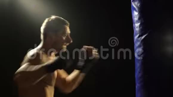 大胡子男拳击手在黑暗的背景下用拳击袋训练年轻拳击手的拳击训练男性拳击手视频的预览图