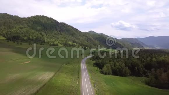 空中飞行在田野和山脉之间的道路上夏日阳光明媚在路上路过汽车阿尔泰共和国视频的预览图