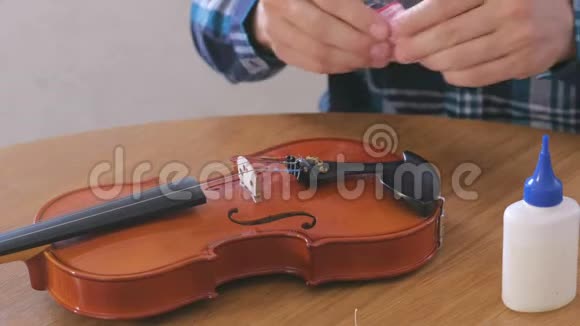 穿格子衬衫的年轻人的特写双手正在修理坐在桌子旁的小提琴用油润滑机构视频的预览图
