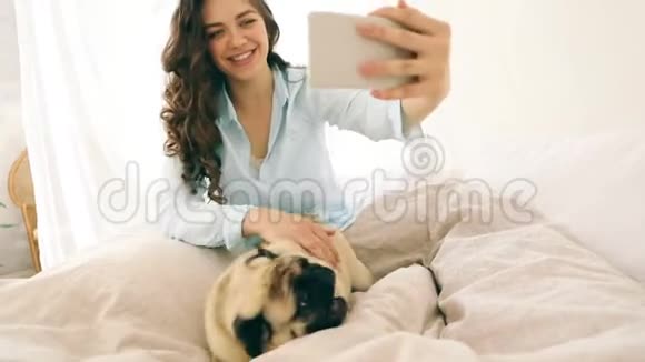迷人的黑发女人在床上自拍与她的小狗pug录像片段周末早上好心情玩游戏视频的预览图