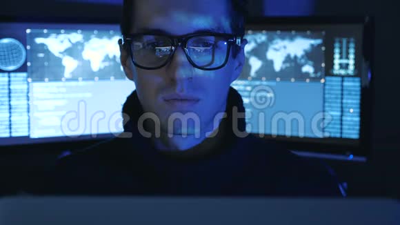 戴眼镜的Hacker程序员的肖像看着摄像机而蓝码字符则在网络中反射他的脸视频的预览图