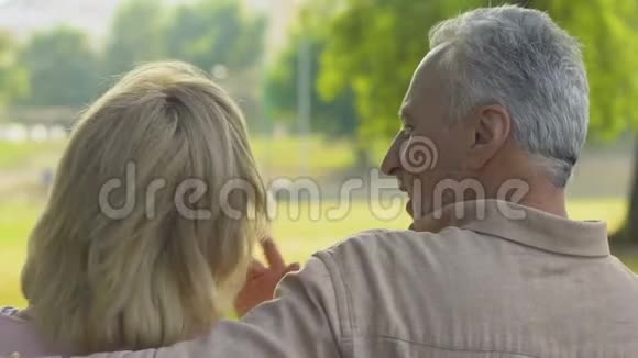 快乐的老人坐在公园的长凳上聊天拥抱后景视频的预览图