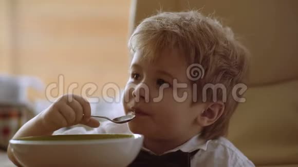 小孩自己用勺子吃粥看动画片小可爱的金发男孩吃粥视频的预览图