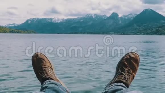 人的双腿在一个山湖和白雪覆盖的山脉的背景上视频的预览图