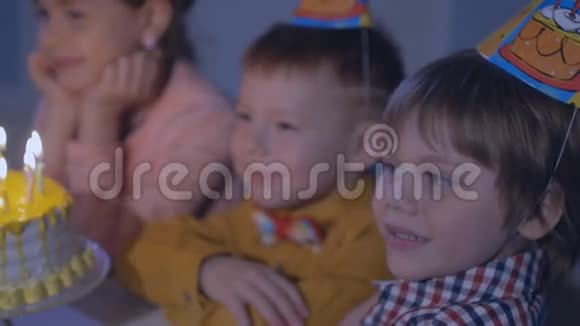 小孩子们端着蛋糕坐在红桌旁在生日聚会上吹着五颜六色的吹箫视频的预览图