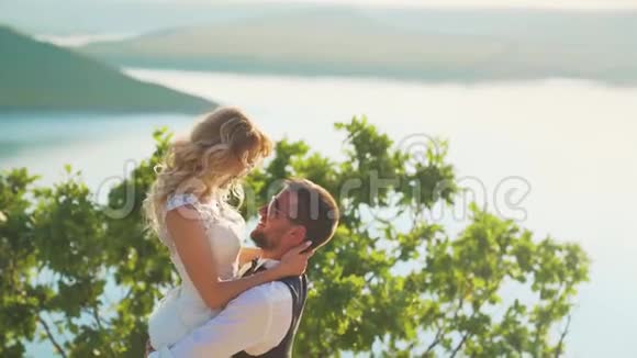 一对夫妇轻轻拥抱站在悬崖边上看着湖面视频的预览图