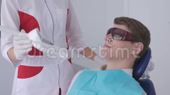 戴着红色防护眼镜的年轻人在牙医那里接受紫外线美白视频的预览图