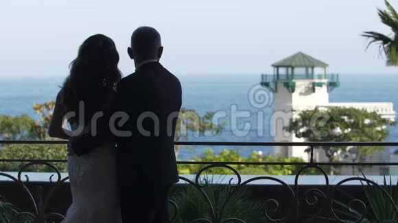 新娘和新郎穿着白色连衣裙从阳台上眺望大海视频的预览图