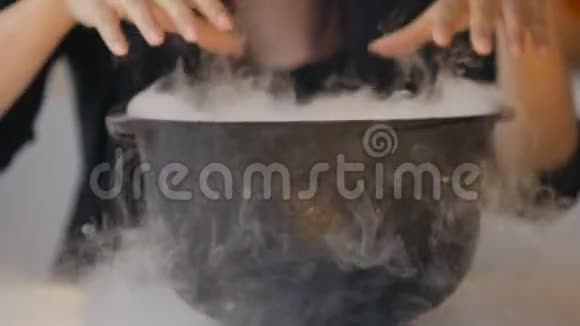 穿着女巫服装的女人用药水在神奇的锅上做魔法手势视频的预览图