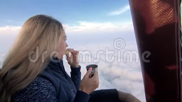女人在飞行中吃三明治喝茶和咖啡在热气球上冒险飞翔在清晨的蓝天之上视频的预览图