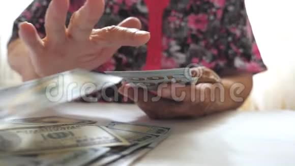 祖母手里拿着一捆钱把一百美元的钞票扔到桌子上老妇人的手臂视频的预览图