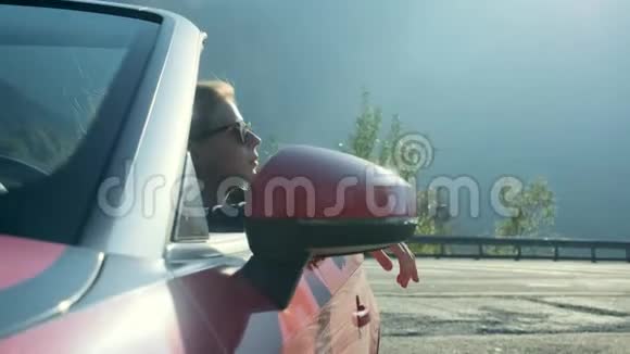 年轻女孩在敞篷车里抽烟年轻漂亮的金发女孩戴着黑色眼镜和皮夹克穿着红色的烟视频的预览图