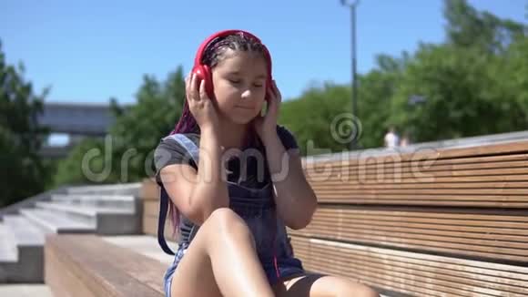 夏天公园坐在长凳上听耳机音乐的女孩慢动作视频的预览图