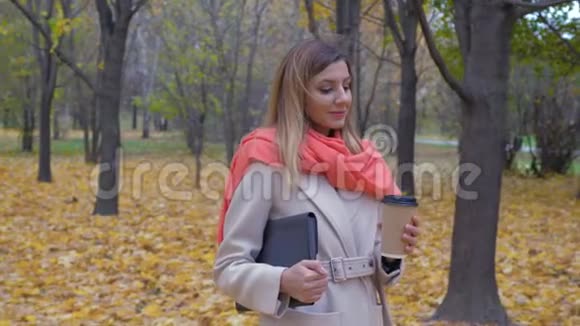 秋天公园里一位优雅的女士拿着文件夹或笔记本电脑喝咖啡视频的预览图