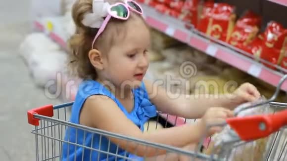 小女孩坐在超市里的小推车里吃东西拿着意大利面婴儿购物视频的预览图