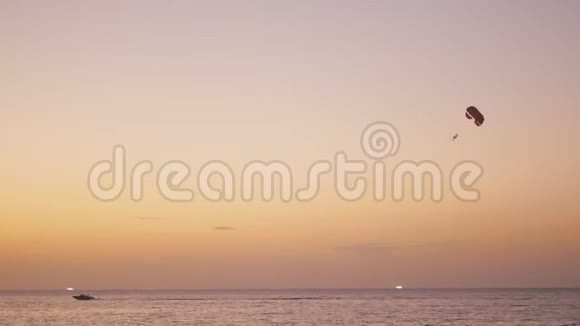 日落后在热带海滩进行降落伞活动与人一起拖着降落伞平静的海水视频的预览图