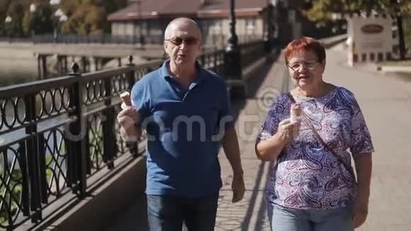 一对老夫妇穿着华夫饼圆锥体吃冰淇淋沿着长廊散步视频的预览图