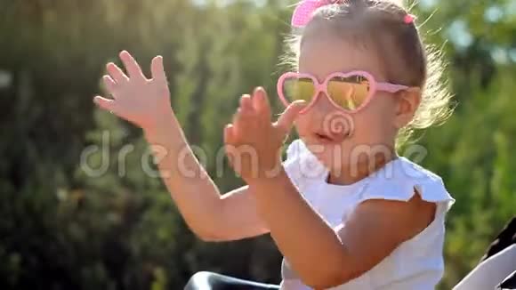 太阳眼镜的孩子在日落时拍手阳光明媚的日子里一个快乐的女婴特写的肖像视频的预览图