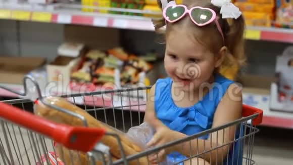 小女孩坐在商店里的手推车里拿着一个面包婴儿购物视频的预览图