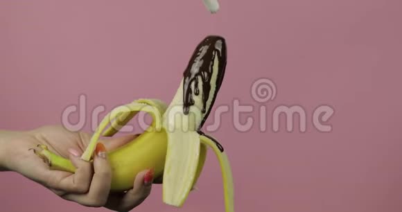 用融化的黑巧克力糖浆浇香蕉粉色背景视频的预览图