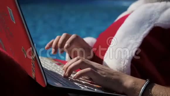圣诞老人手在泳池附近的笔记本电脑键盘上打字视频的预览图