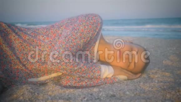 穿着睡衣的女孩在日落时分在海滩上打瞌睡被夕阳照亮视频的预览图