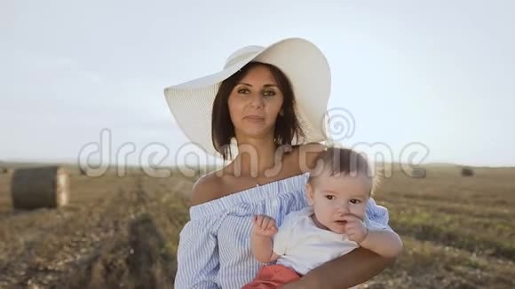 一个年轻漂亮的女人戴着一顶大帽子她的小儿子戴着一个白色的身体站在一个金色的视频的预览图