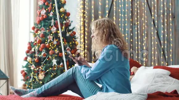 漂亮的金发女孩坐在家里的沙发上在手机上发短信视频的预览图