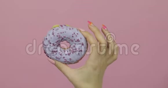 女人手里拿着蓝色的美味的洒在粉红色背景上的甜甜圈视频的预览图