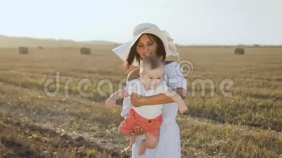漂亮的年轻妈妈戴着大帽子穿着轻薄的连衣裙和小男孩在田野上玩着包小妈妈视频的预览图