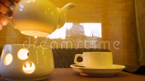 男子手拿水壶站在蜡烛上在茶杯特写中倒热茶视频的预览图
