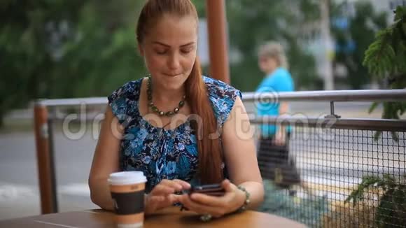 一个红头发的漂亮女人坐在街头咖啡馆的桌子旁喝咖啡视频的预览图