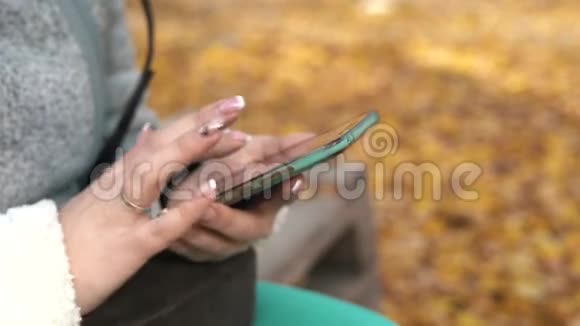 在秋季公园用智能手机端坐在长凳上把女人的手收起来视频的预览图
