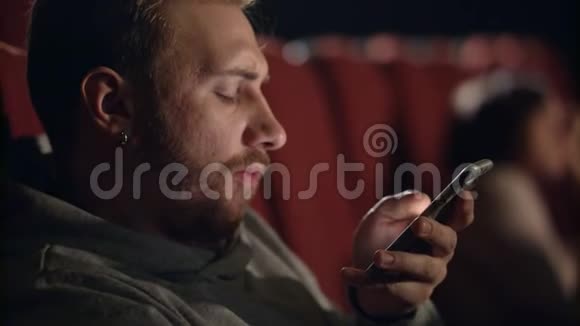 打哈欠的人在电影院里用智能手机看无聊电影的年轻人视频的预览图
