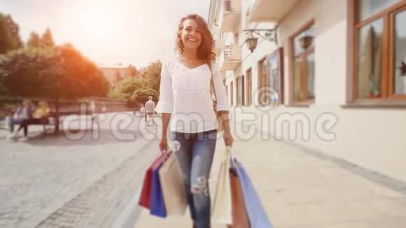 快乐的女人带着购物袋在城里散步慢动作阳光背景视频的预览图