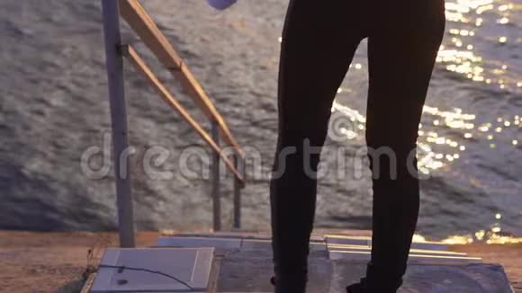 下面的动作一个穿着夹克衫和运动裤的年轻女人走下楼梯来到一个大湖的水上视频的预览图