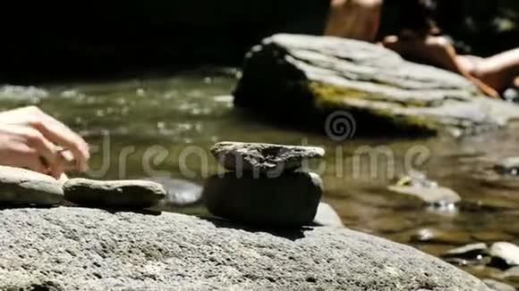 在游客的背景下人类把一个婴儿放在山河的鹅卵石上视频的预览图