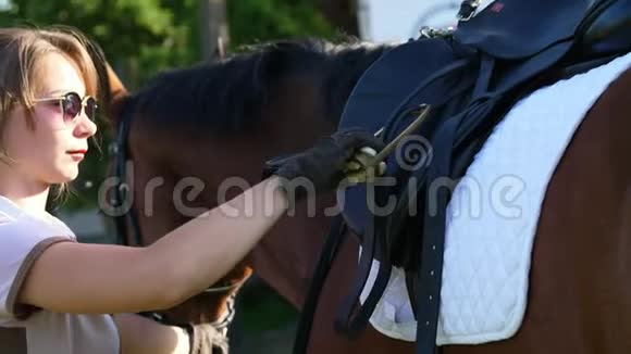 一个年轻的女孩一个骑手一个骑师调整马鞍上的马镫为骑马课程准备一匹马视频的预览图