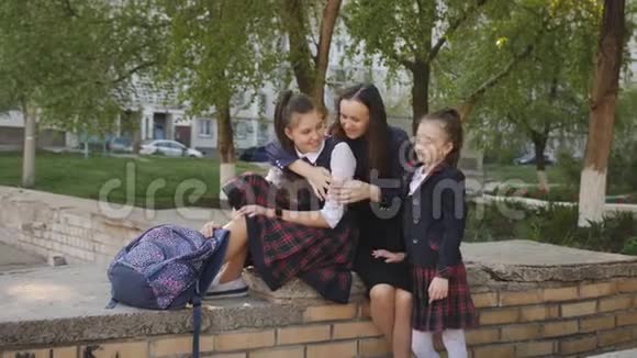 母亲带着两个穿校服的女儿背着背包坐在学校附近的街道上聊天视频的预览图