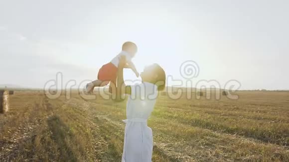 年轻的女人带着小宝宝在田野里玩得很开心在日落的时候夏天的晚上穿裙子的可爱妈妈视频的预览图